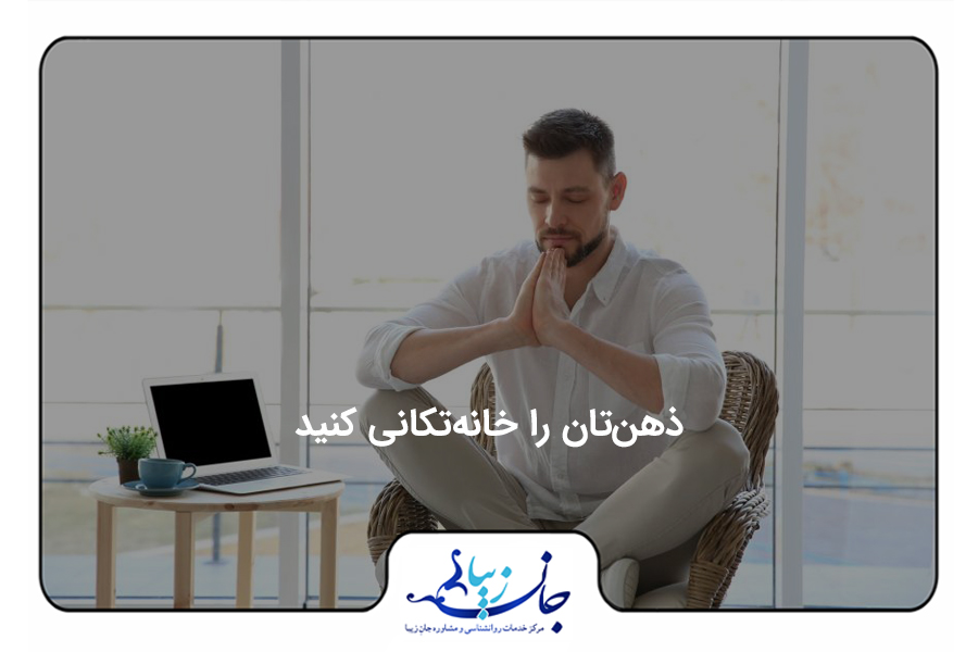 مردی به صورت چهارزانو روی مبل نشسته، چشمان خود را بسته و دست‌های خود را به صورت یوگا روبروی صورتش گرفته. در کنارش روی میز یک لپتاپ و گلدان قرار دارد